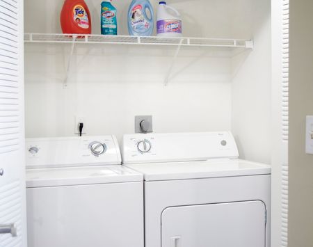 In-unit washer and dryer machines located inside of double-door closet. Overhead wire shelving holding laundry detergents