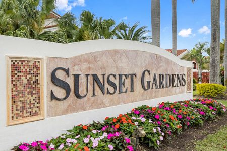 Stone monument sign placed reads Sunset Gardens, located outdoors in a flower bed near the entrance driveway