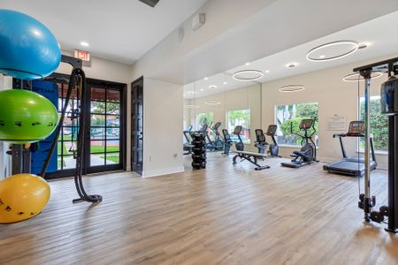 Brand New Fitness center with mirrored wall, strength training equipment, and treadmills. Flat screen televisions above large windows with view of community areas