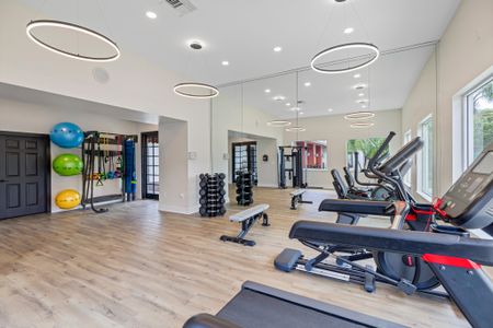 Fitness center with mirrored wall, strength training equipment, and treadmills. Flat screen televisions above large windows with view of community areas