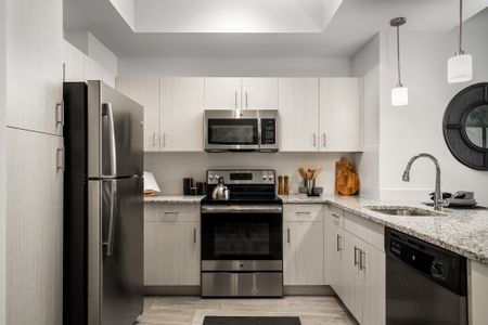 Apartment kitchen with porcelain tile flooring, pendant lighting, peninsula granite countertop, stainless steel appliances including a refrigerator, dishwasher, microwave and an oven and stove combo, and an undermounted single basin sink