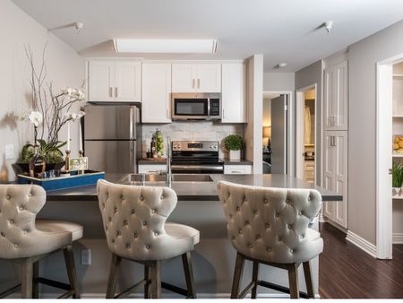 kitchen with stainless steel appliances and wood-inspired plank flooring and quartz countertop and three beige bar chairs at at the warwick