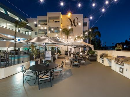 Pool deck with cabanas and lounge seating, tables and bbq grill at night at the warwick