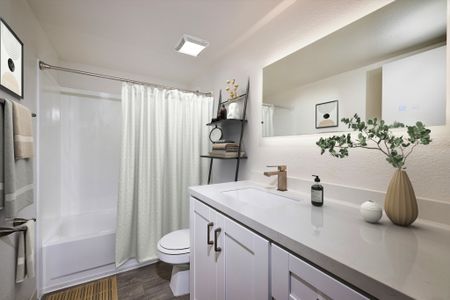 Updated bathroom with wood-inspired plank flooring, new white cabinets, shower/tub combo, and quartz countertops