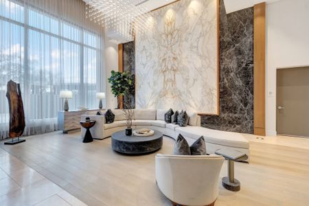 Spacious lobby with a long curved couch, high ceilings, full-width floor-to-ceiling windows, modern art, and a full-height book-matched marble focal piece on the wall.