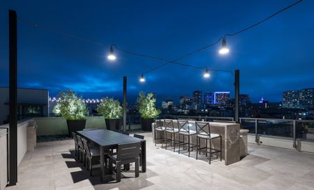 Rooftop open-air lounge overlooking the city skyline with a wooden dining table and a grilling station with granite countertops and bar-style seating