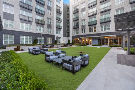 Outdoor courtyard with large grass area, 2 tables and upholstered patio-style chairs.
