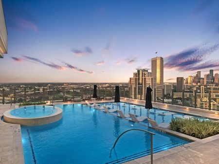 A rooftop pool at dusk, with multiple seating and dining areas, lounge chairs, a hot tub, and a city skyline view.