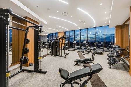 Bank of treadmills, ellipticals, and stair climbers in front of a large window wall with a city skyline view.