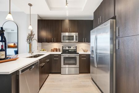 Chef-inspired kitchen with warm wood-style floors, dark wood cabinets, stainless steel appliances, granite countertops, and a recessed ceiling