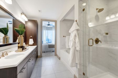 En-suite bathroom with a frameless glass walk-in shower, large bathtub, stone floors, and stone-topped dual vanity