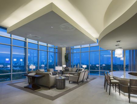 Lounge featuring white ceilings, floor-to-ceiling windows, seating area with gray couches and chairs, and a bar area with gray and brown barstools.