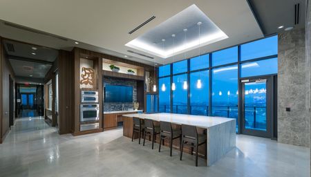 Entertaining and catering kitchen with double ovens, stone floors, a sizeable marble 8-person dining table and island, a terrace, and a city view through floor-to-ceiling windows