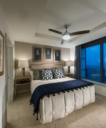 Spacious carpeted bedroom with a king-sized bed, full-width window, recessed ceiling with a fan, and a taupe accent wall