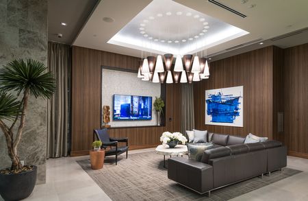 A long brown leather sectional couch and armchair in front of an HDTV in a room with wood-paneled walls and a bold modern chandelier