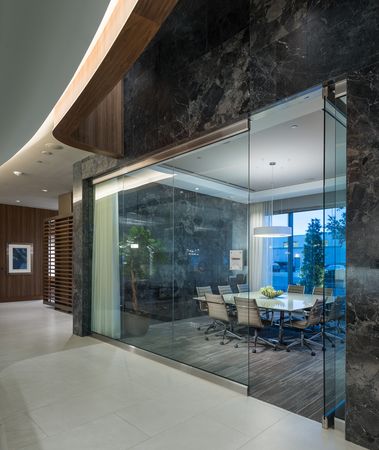 A square conference table with rolling leather chairs in an impressive room with black marble walls and full-width floor-to-ceiling interior and exterior glass walls.