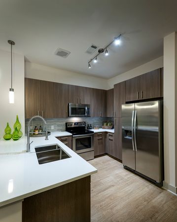 A kitchen with pine wood-style floors, modern dark wood-style cabinets, stainless steel appliances, and a white quartz peninsula.