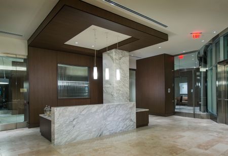 Marble concierge desk in a spacious lobby with floor-to-ceiling windows, stone floors, and wood-paneled walls.