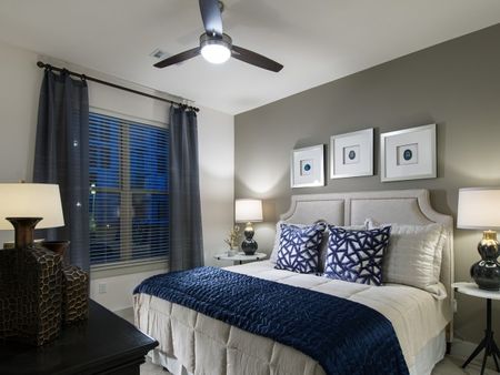 A bedroom with a king-sized bed, ceiling fan, large window, and white walls with a gray accent wall.