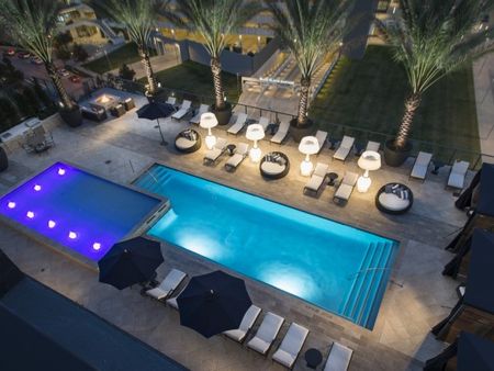 Overhead view of elevated pool deck with cabanas, grilling station, fire pit, hot tub, palm trees, and lounge chairs.