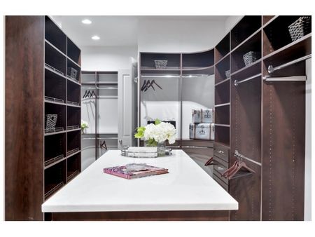 Vast walk-in closet with built-in shelves and closet rods across three walls and a stone-topped dressing table