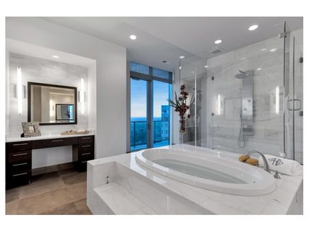 Vast bathroom with a marble-clad step-up oval bathtub, large frameless walk-in shower, and sliding door out to a balcony