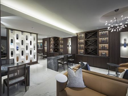 Resident lounge with leather couches, black marble desks, white marble floors, a geometric white room divider, and a wood-paneled wall of wine bottles stored behind gold grates.