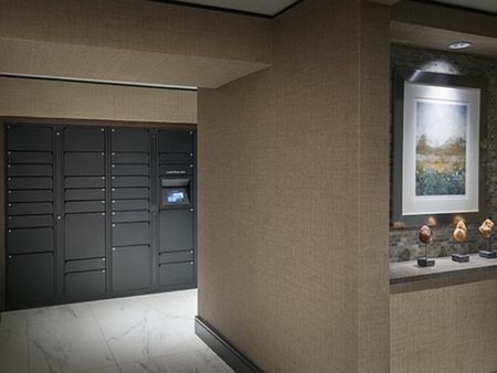 An around-the-corner glimpse of the package room, with marble floors, gray lockers of various sizes installed along the wall, and a touch-screen access panel.