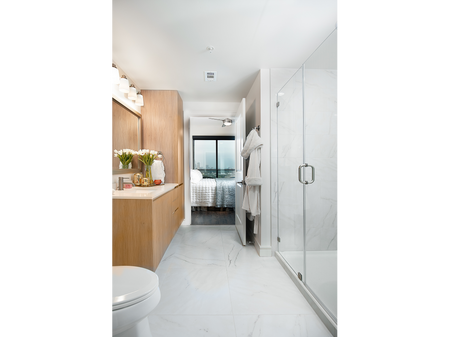 Spacious bathroom with walk-in glass shower, white marble floors and tiling, light wood cabinetry and a large vanity area with a white marble countertop.