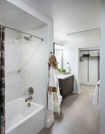 Spacious bathroom with an attached walk-in closet, tile floors, and a large bathtub with marble tile walls