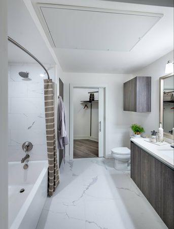 Bathroom with a large tub, dark wood cabinets, an attached walk-in closet, and marble tile on the floor and bathtub walls