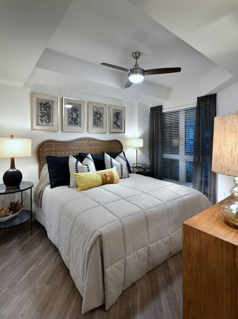 Bedroom with wood-style floors, large window, recessed ceiling with a fan, king-sized bed, two nightstands, and a dresser