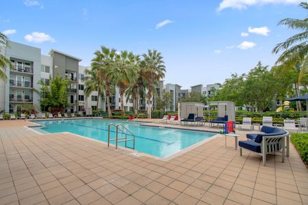 Studios in Delray Beach, FL - Congress Grove - Pool with Lounge Chairs, and Patio Furniture, Surrounded by Trees.