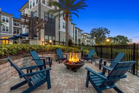 Outdoor fire pit with blue wooden chairs surrounding it in the nighttime with apartments in the background