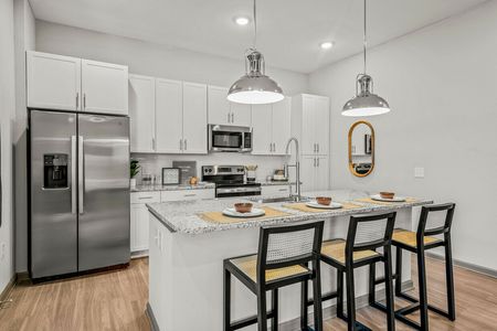 Pinellas Park, FL Apartments - Rowan Pointe - Modern Kitchen With Granite Counters, White Cabinetry, And Stainless Steel Appliances With An Island Bar and Wood-Style Flooring