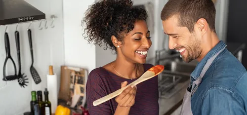 man and woman cooking and tasting meal together in kitchen