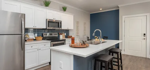 Bright and contemporary kitchen featuring white cabinets, stainless steel appliances, and a chic bar counter.