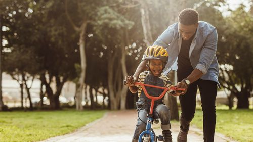 man helping young boy on bicycle outside in park in daytime