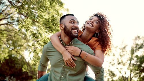 Man giving woman piggy back ride laughing outside
