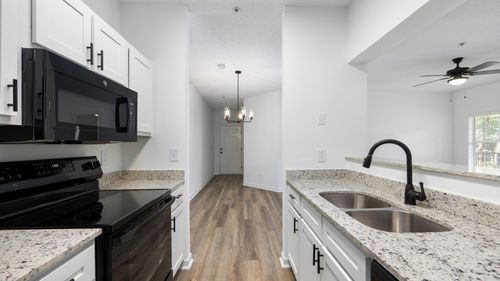 Galley kitchen with white cabinets, wood style flooring and black appliances