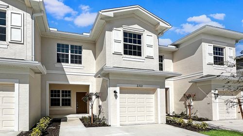 Charming townhouse with elegant facade, featuring large windows and a private driveway, surrounded by lush landscaping under a clear blue sky.