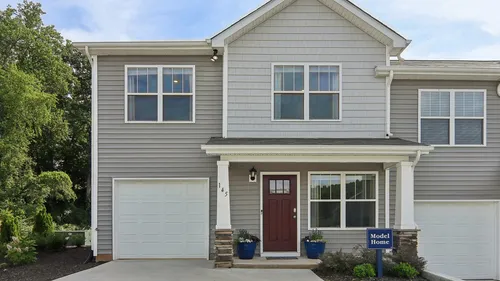 Charming two-story townhouse with elegant gray siding, a welcoming red front door, and manicured landscaping, perfect for modern living.