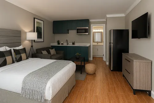 Modern studio apartment featuring a cozy bed, stylish kitchenette with teal cabinets, comfortable seating area, and sleek decor.