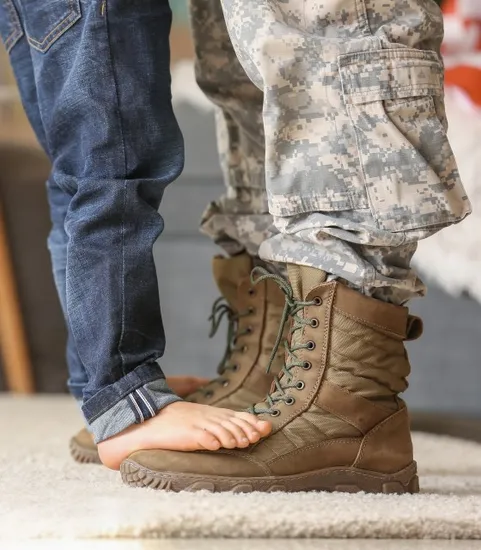 kids feet resting on pair of soldier's feet on ground