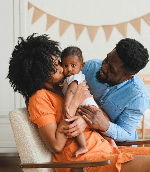 mom and dad kissing baby on the cheek in nursery room
