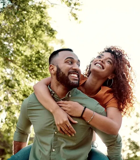man holding woman on his back in a park outside