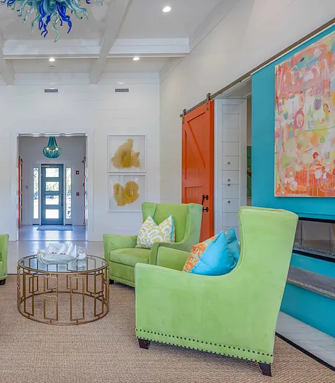 Bright and stylish living area with lime green armchairs, a glass table, colorful art, and modern lighting.