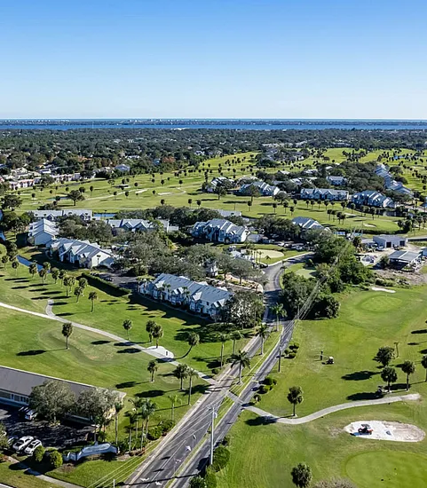 Scenic aerial view of a sprawling golf course surrounded by residential community under a clear blue sky.