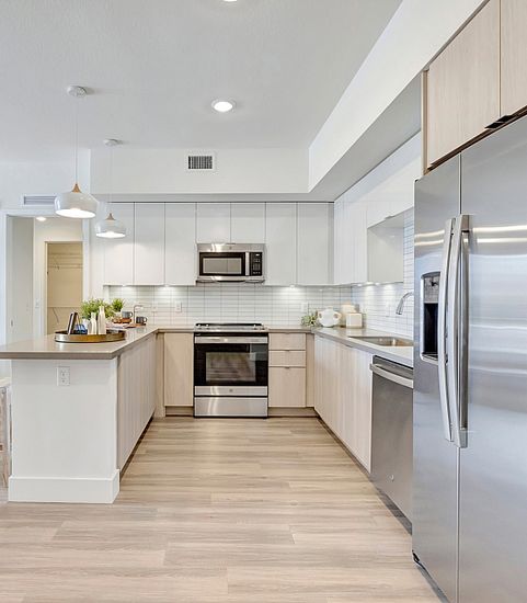 Contemporary open kitchen and living area with sleek stainless steel appliances, stylish pendant lighting, and modern decor for a cozy, inviting atmosphere.
