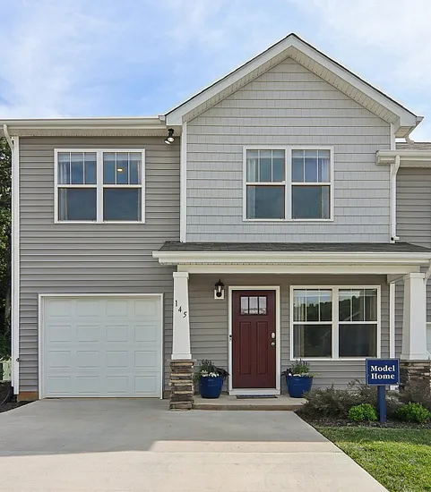 Charming modern townhouse with a welcoming front porch, stylish grey exterior, and attached garage, set against lush greenery, perfect for comfortable living.